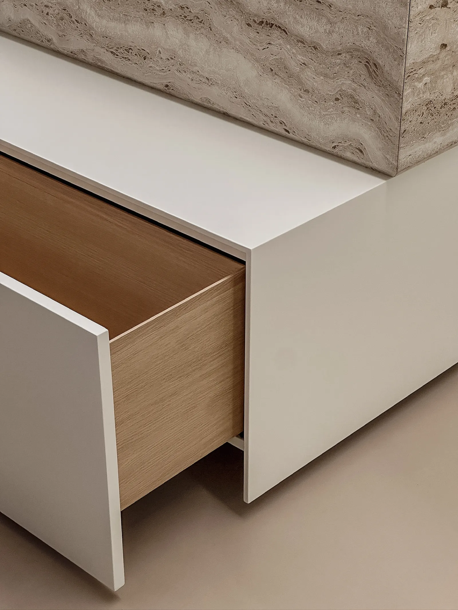 Un cassetto in rovere si apre da un volume laccato sotto un piano in travertino