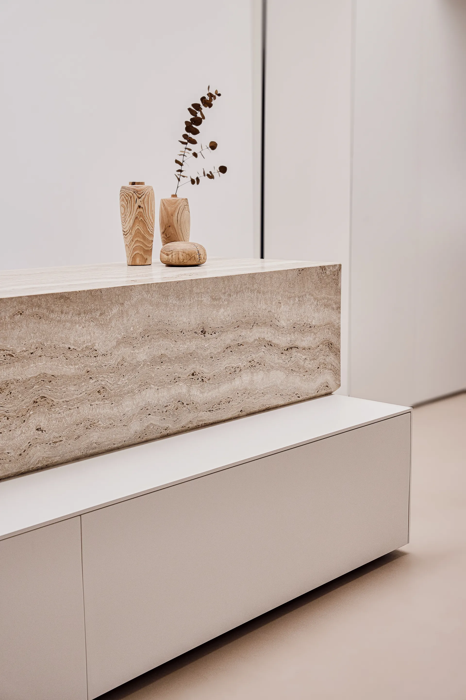 L'isola OR1 vista di lato: il volume in travertino sospeso sul rovere con i vasi torniti appoggiati